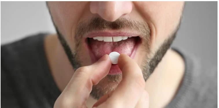 A man placing a small pill on his tongue