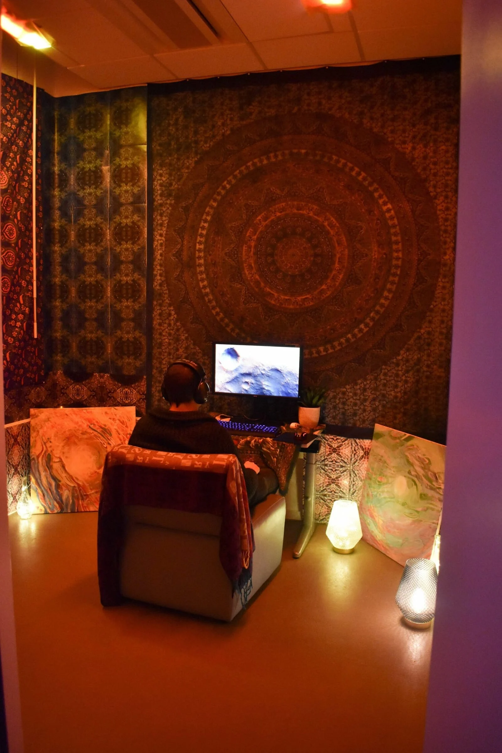 A dimly lit, lounge-style experiment room with a tapestry, cushions and candles