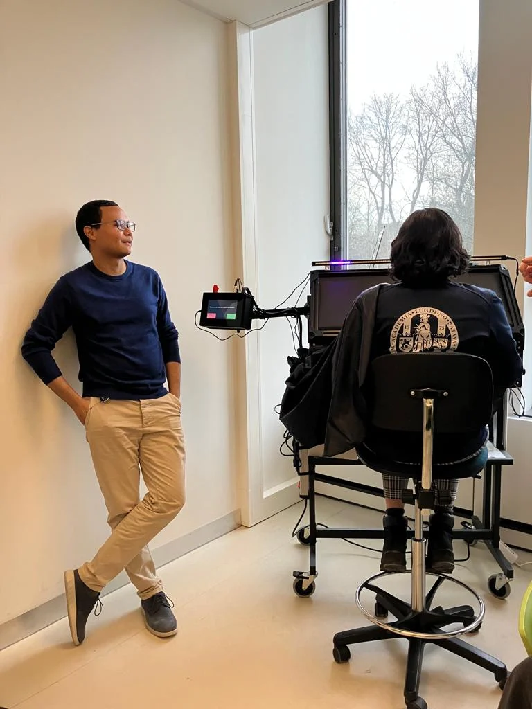 A researcher next to a participant seated in a lab set-up